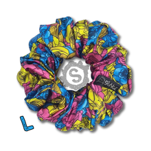 Load image into Gallery viewer, A large colourful scrunchie. A rose pattern in the colours of the Pansexual pride flag. Blue, pink and yellow. Approximately 12cm in Diameter.
